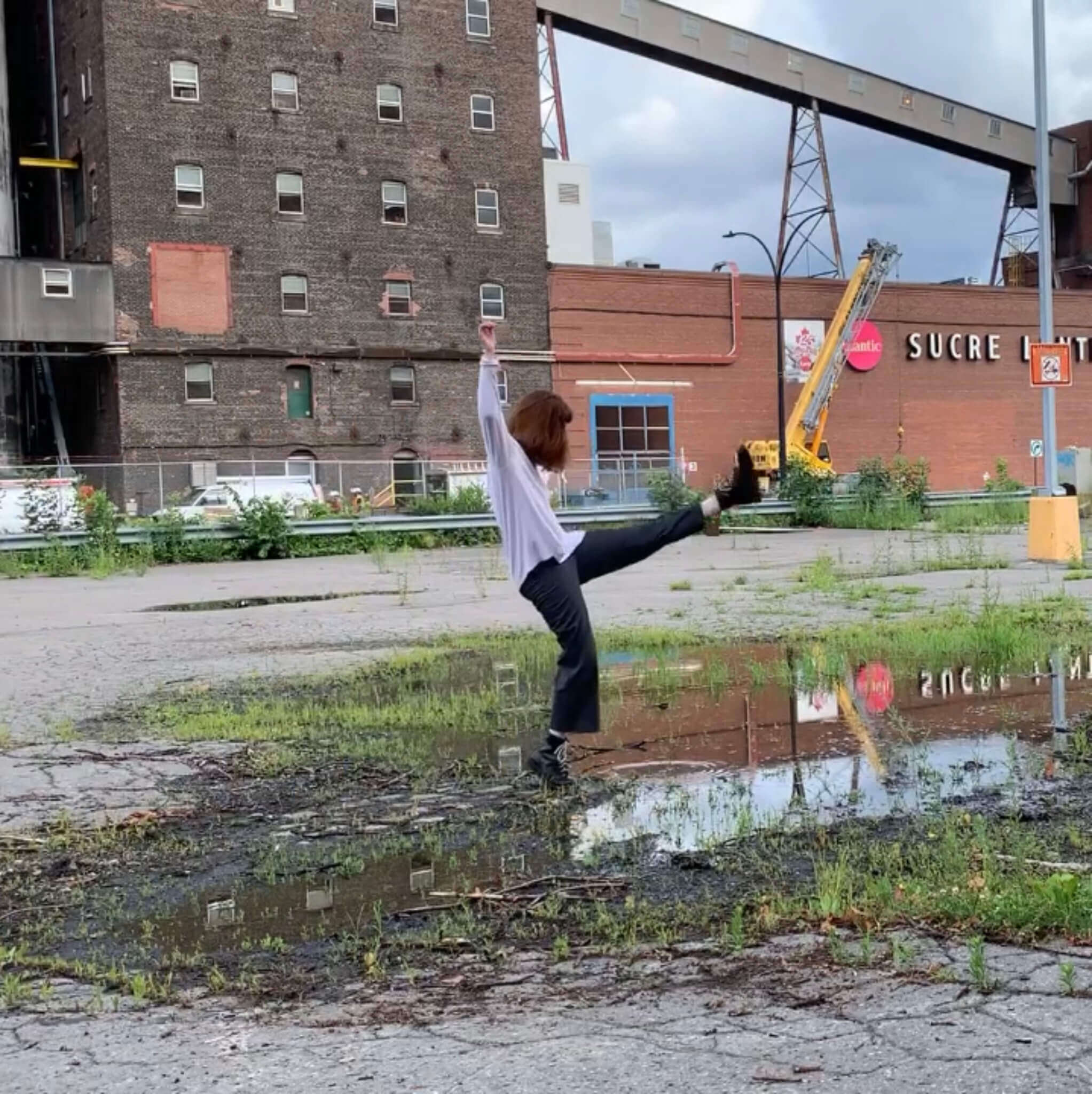 L'interprète en danse Molly Siboulet-Ryan donne un coup de pied dans les airs, devant une usine à sucre.