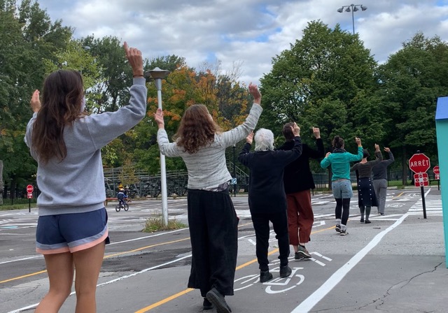 Des danseurs dansent l'un derrière l'autre dans une ligne. Ils sont dans un parc.