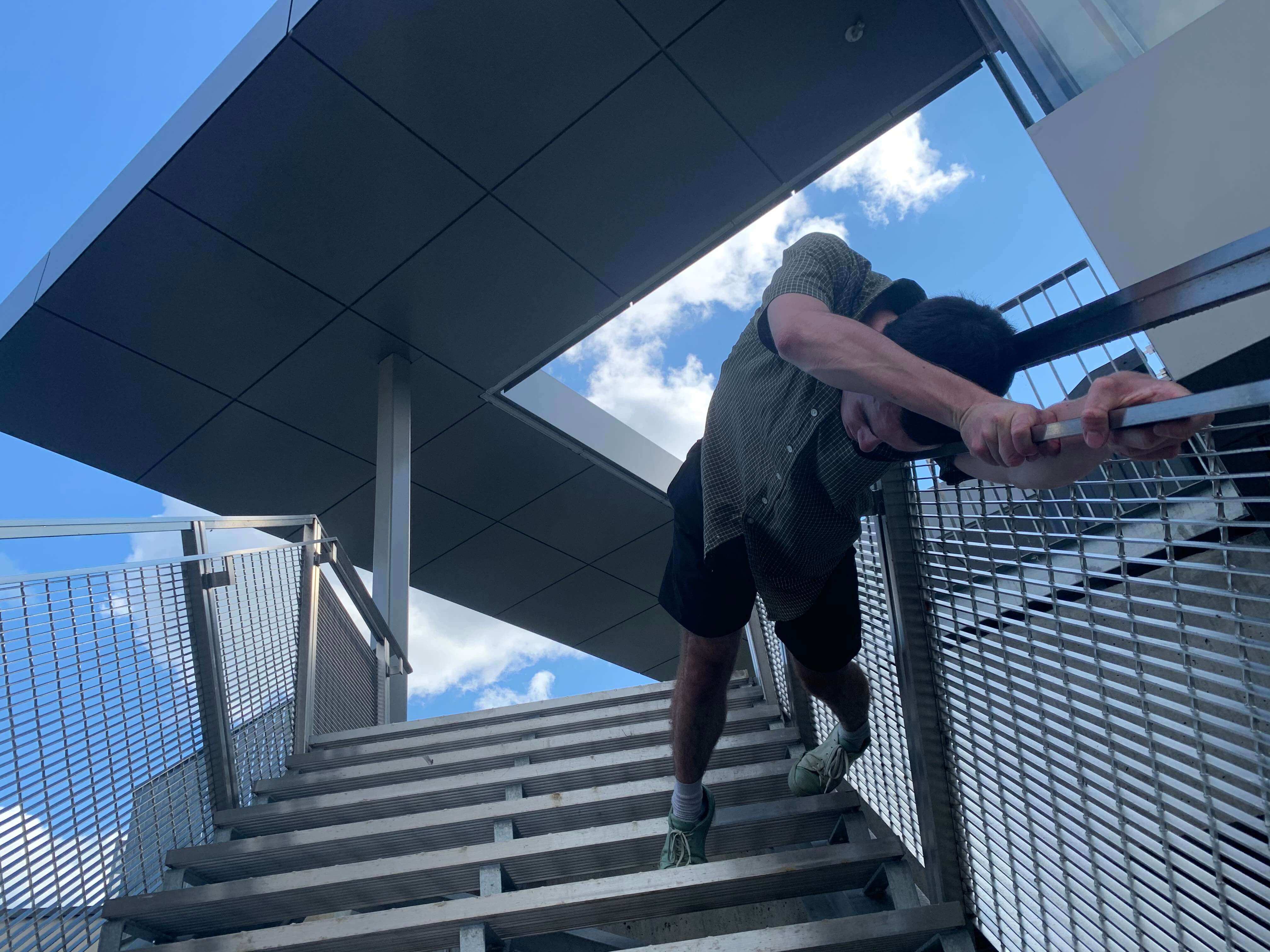 L'interprète en danse Philippe Dépelteau, en contre-plongé, est allongé sur une rampe d'escalier.