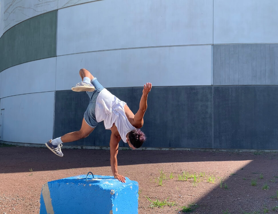 L'interprète en danse Rodrigo Alvarenga fait un équilibre sur les mains sur une petite plateformme à l'extérieur.