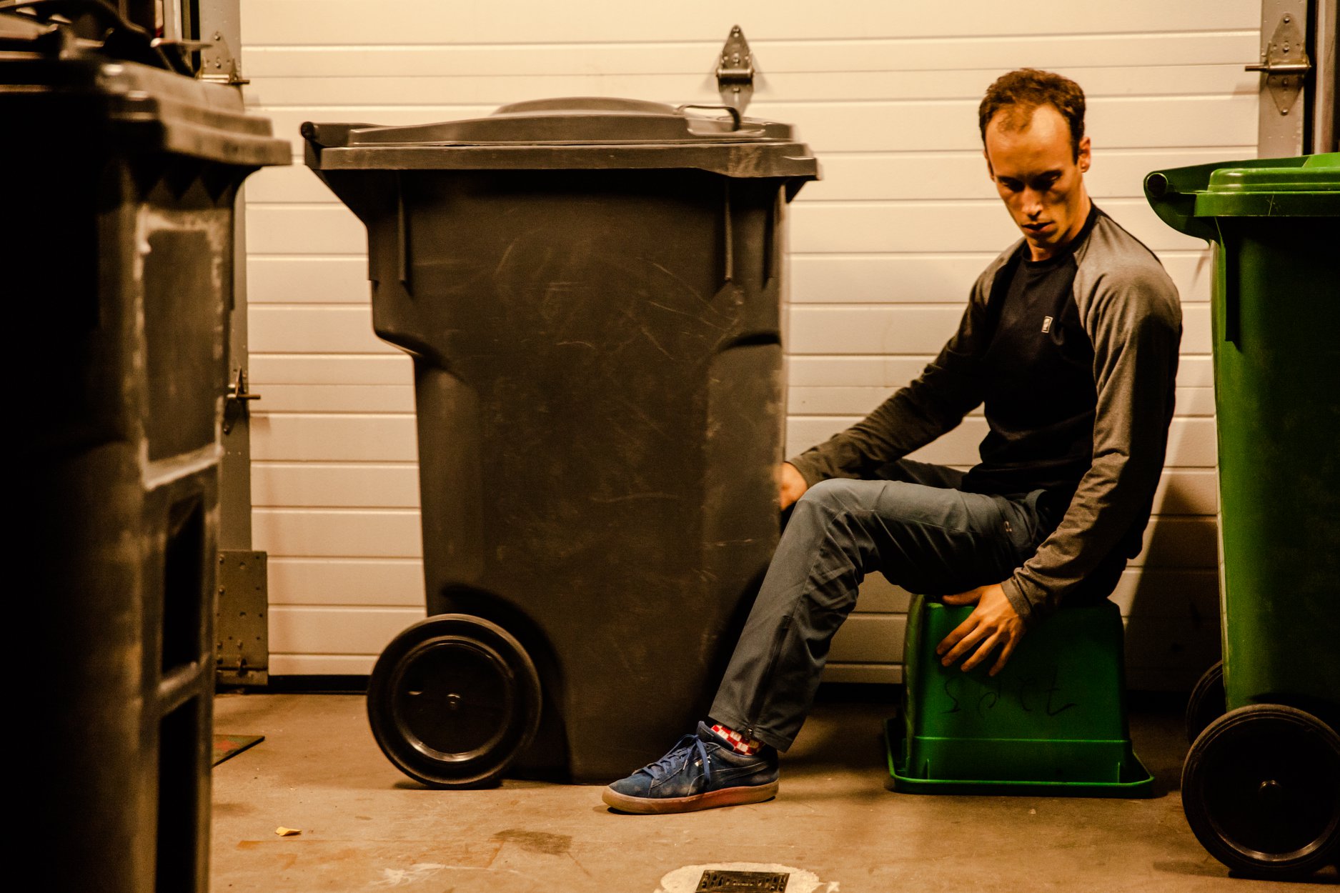 Guillaume Loslier-Pinard, danseur, assis sur un bac à recyclage, dans un garage, regarde vers le sol.