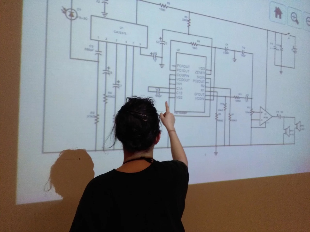 Une personne pointe une grande projection sur le mur d'un schéma de circuit imprimé.