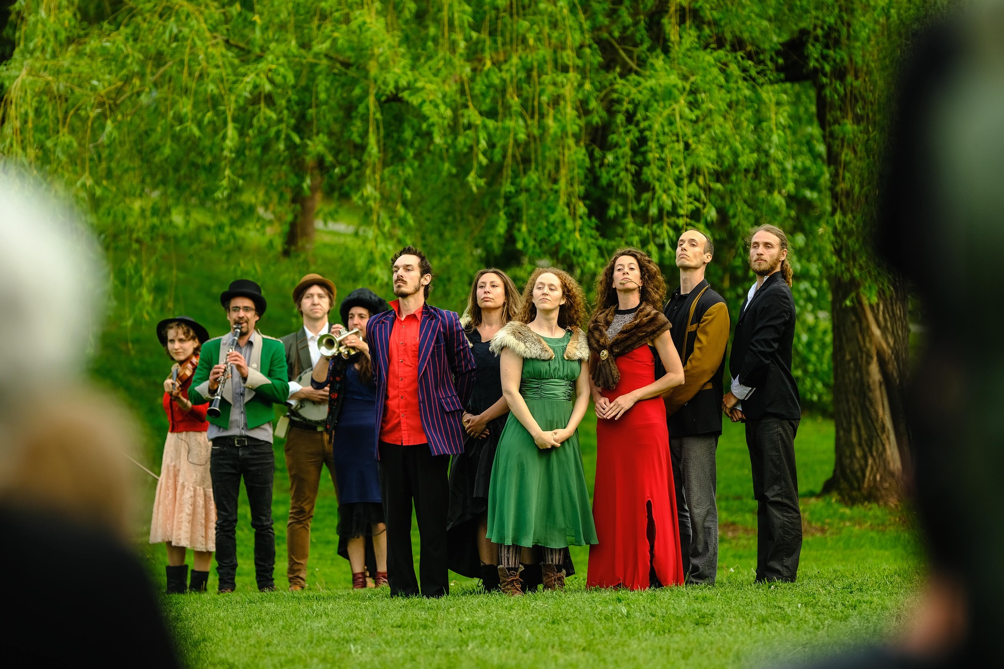 A group of musicians and dancer fancily dressed in a park.