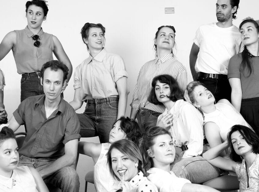 A group of dancers dressed in 50's fashion pose for the camera, relaxed.